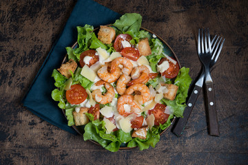 Traditional Caesar salad with shrimp, Parmesan and croutons on a dark wooden background.