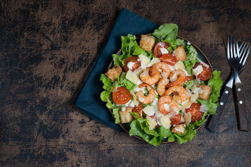Traditional Caesar salad with shrimp, Parmesan and croutons on a dark wooden background.