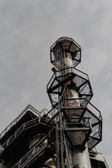 Fototapeta na wymiar Ladders and expanded metal walkways around a smokestack, urban industrial steel mill, vertical aspect