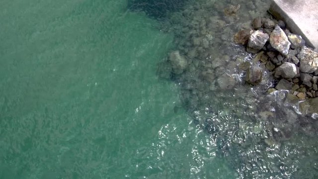 Aerial view of stunning turquoise sea in the summer with pier and rocks that water pops up on them in the area of Agia Paraskevi Halkidiki, Greece, up and side movement by drone