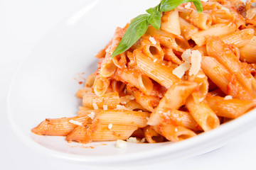 Penne with pesto rosso and sun dried tomatoes decorated with basil on a white background