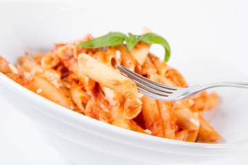 Penne with pesto rosso and sun dried tomatoes decorated with basil eaten with a fork