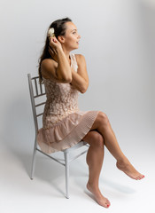 Horizontal portrait full length sitting on a white chair on a white background beautiful pretty woman in a fashionable light pink dress, in various poses. Stylish trendy youth.