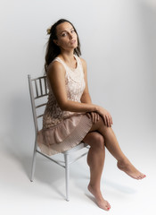 Horizontal portrait full length sitting on a white chair on a white background beautiful pretty woman in a fashionable light pink dress, in various poses. Stylish trendy youth.