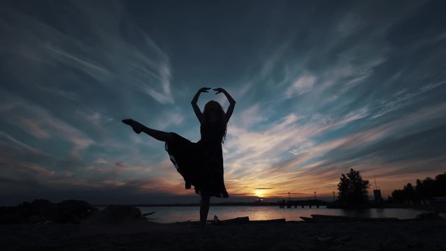 young girl dancing gracefully against the backdrop of the sunset. silhouette of a ballerina in a flying dress.