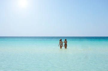 Back view of two beautiful friendly women bathing in the clear sea against a sunny sky.Vacation...
