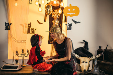 31 october. Magic hat. Best ideas for Halloween. Mother and child boy playing together. Mother wearing as witch, son wearing as devil. Mom and son play for all saints day in witch's costume at home.