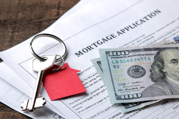 mortgage application. Key with red keychain house and blank and money on a brown wooden table....