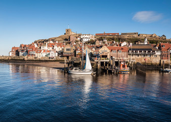 Whitby harbour on a clear day showing the quayside and the church on the hill with a boat moored by the side of Whitby’s life boat. 