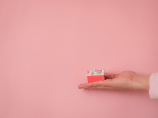 Hand with a gift on pink background with copy space