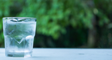 Glass with ice put on table green background of nature.