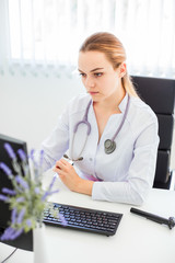 Young smiling doctor sitting at the desk on a black chair with her arms crossed