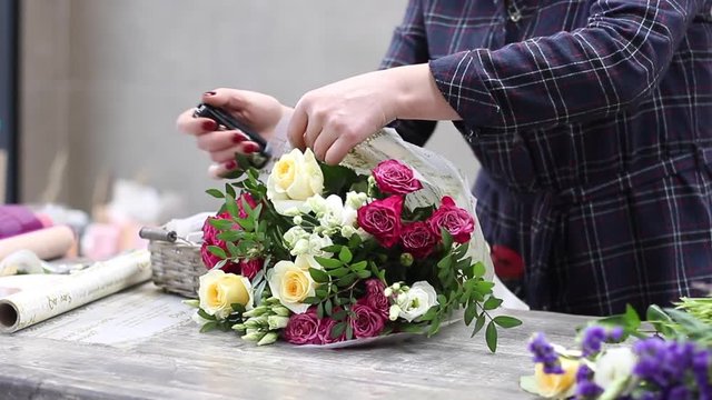 Female florist arranging flowers in flower shop. Florist packing bouquet with bouquet cover paper