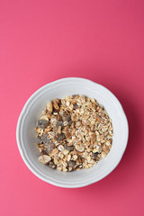 A plate of delicious muesli on a bright pink background, top view. Muesli consist of a blend of multigrain flakes with dried fruit, nuts and sunflower seeds.
