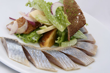 Herring fish with potatoes slices, greens, red onion and rye bread on the white background. 