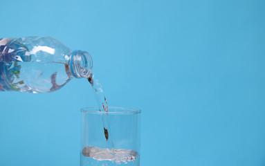Closeup of pouring mineral drinking water from plastic bottle into glass with blue background. 