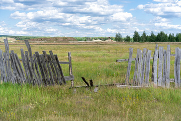 old wooden rickety fence. Abandoned field with an old wooden fence. Old broken wooden fence. Summer sunny day with blue sky and white clouds. the effects of the hurricane. Disaster