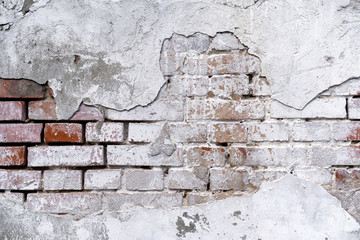 brick wall background with white fallen off plaster. The brick wall is visible from under the white plaster. White stucco and brick wall texture. piece of brick wall under plaster