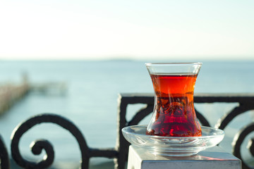Traditional Turkish black tea in a glass and a blurred sea in the background.