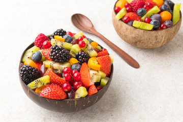Colourful fruit salad in a coconut bowl and wooden spoon white  stone surface