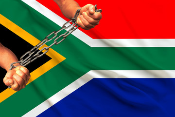 male hands chained in heavy iron chains against the backdrop of the flag of South Africa on a...