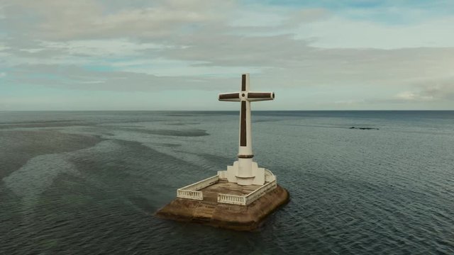 Catholic cross in sunken cemetery in the sea at sunset, aerial drone. Large crucafix marking the underwater sunken cemetary, Camiguin Island Philippines.