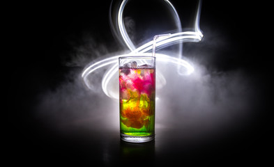 Cocktail glass splashing on dark toned smoky background or colorful cocktail in glass. Party club entertainment. Mixed light.