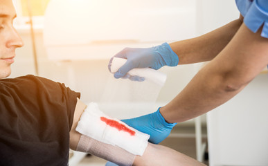 Nurse dressing wound for patient's hand with deep skin cutting.
