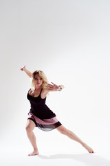 Fototapeta na wymiar Long-haired blonde dancer looking to side with arms stretched back dancing in empty studio