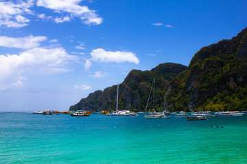 Port with sailboats in a lagoon with clear blue sea water on a background of wild rocks in Thailand. Turquoise sea, blue sky and boats near the rocks on the Islands.