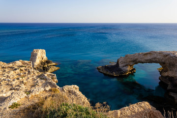 Beautiful view of the blue Mediterranean sea and the rock arch on a Sunny day from Cape Greco in Cyprus. Stone landscape of Ayia NAPA. Yellow rocks in the sea.