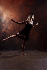 Full-length photo of dancing blonde woman looking in side in short black dress on brown background