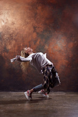Photo of long-haired blonde dancer looking back in torn jeans and sneakers on dark brown background
