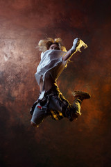 Naklejka na ściany i meble Photo of jumping long-haired blonde in torn jeans on brown background