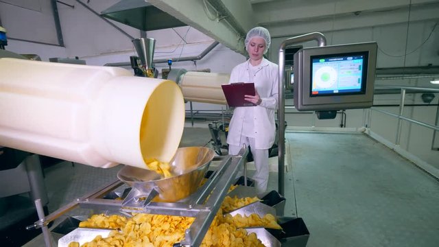 One woman checks work of automated conveyor, moving chips into a container.