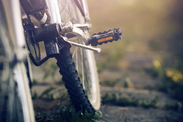The rear wheel of a dirty country bike that stands near the grass in the summer lit up with pleasant light.