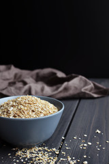 Rolled oats in ceramic bowl on dark wooden background, copy space