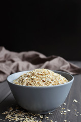 Rolled oats in ceramic bowl on dark wooden background, copy space