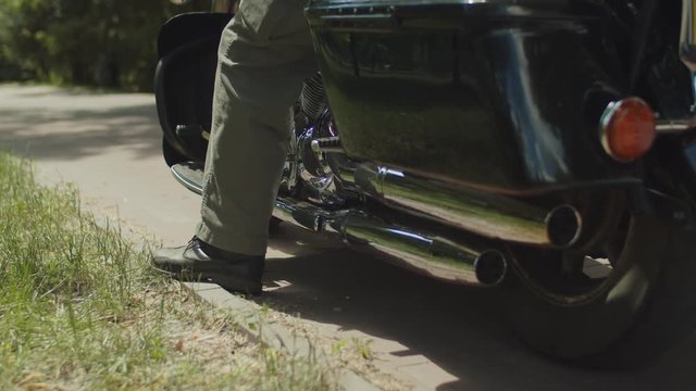Low section of bikers leather boots on a motorcycle pedal before ride. Close-up of bikers leg in motorcycle boots sitting on chopper, starting engine and ready for driving on motorbike.