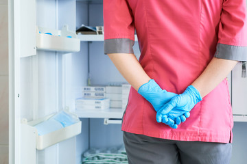 Back view of physician or nurse in pink coat and blue gloves selects pills in the medicine Cabinet.