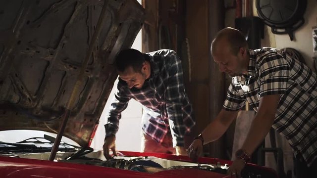 Two mechanics in garage repair car engine in the workroom 