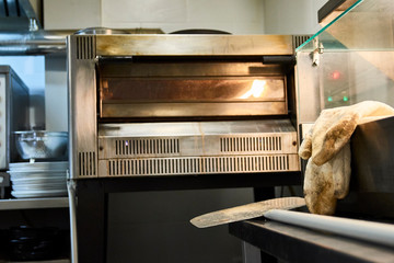 Professional pizzeria kitchen stove appliance: oven, gloves and shovel. Metallic clean stainless. pizzeria interior - obrazy, fototapety, plakaty