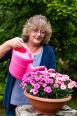 Blonde Frau arbeitet im Garten mit Blumen und Gießkanne