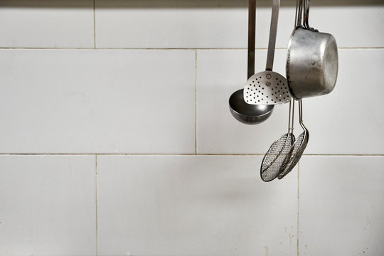 Metallic restaurant utensils hanging above the stove. Used kitchenware.