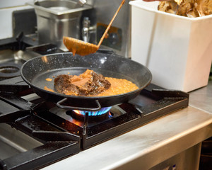 Cook pouring broth into a cooking pan to prepare a delicious paella foundation before pouring the rice.