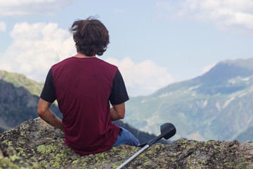 Young hiker in blue pants and shirt is sitting on cliff's edge and looking to misty hilly valley...