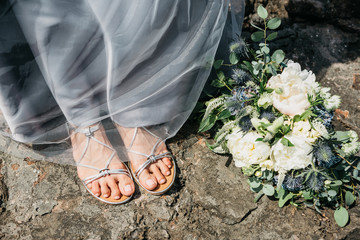 The legs of the bride are in a dress and the wedding bridal bouquet is next on the ground.