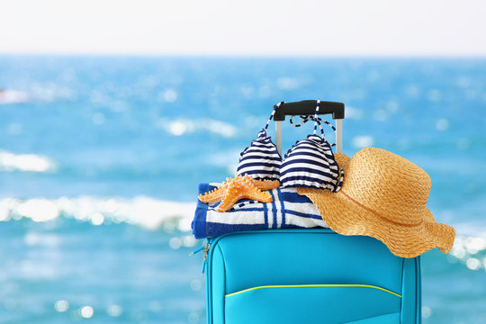 holidays. travel concept. blue suitcase with female hat, starfish, bikini and beach towel in front of tropical background