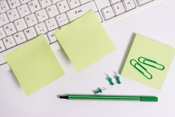 Empty green note paper and paper clips with pencil on the white background and pc keyboard.