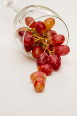 Glass of red grapes on neutral background. Red grapes falling from the wine glass